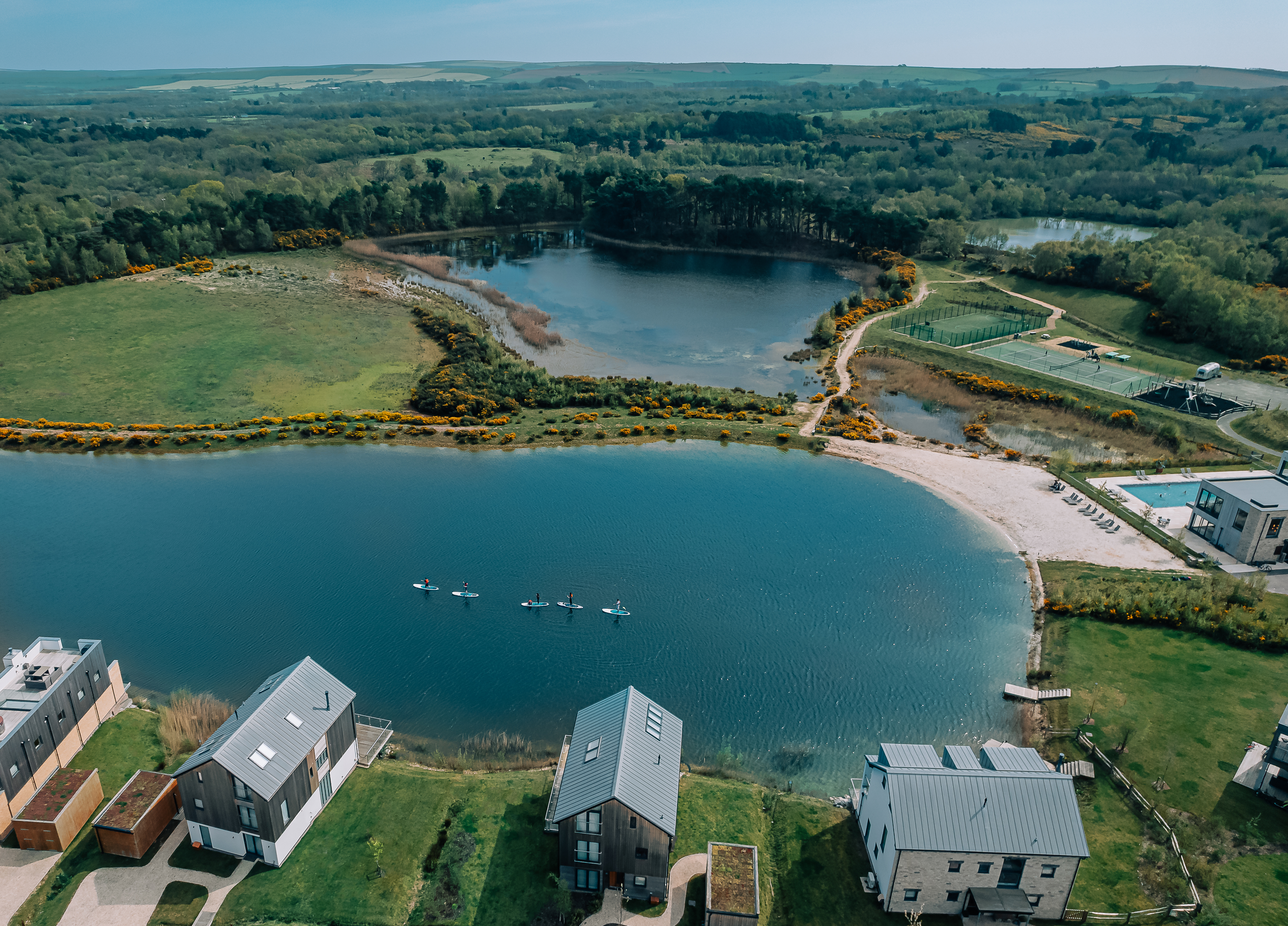 An aerial view of a lake with lodges around it and forests in the distance